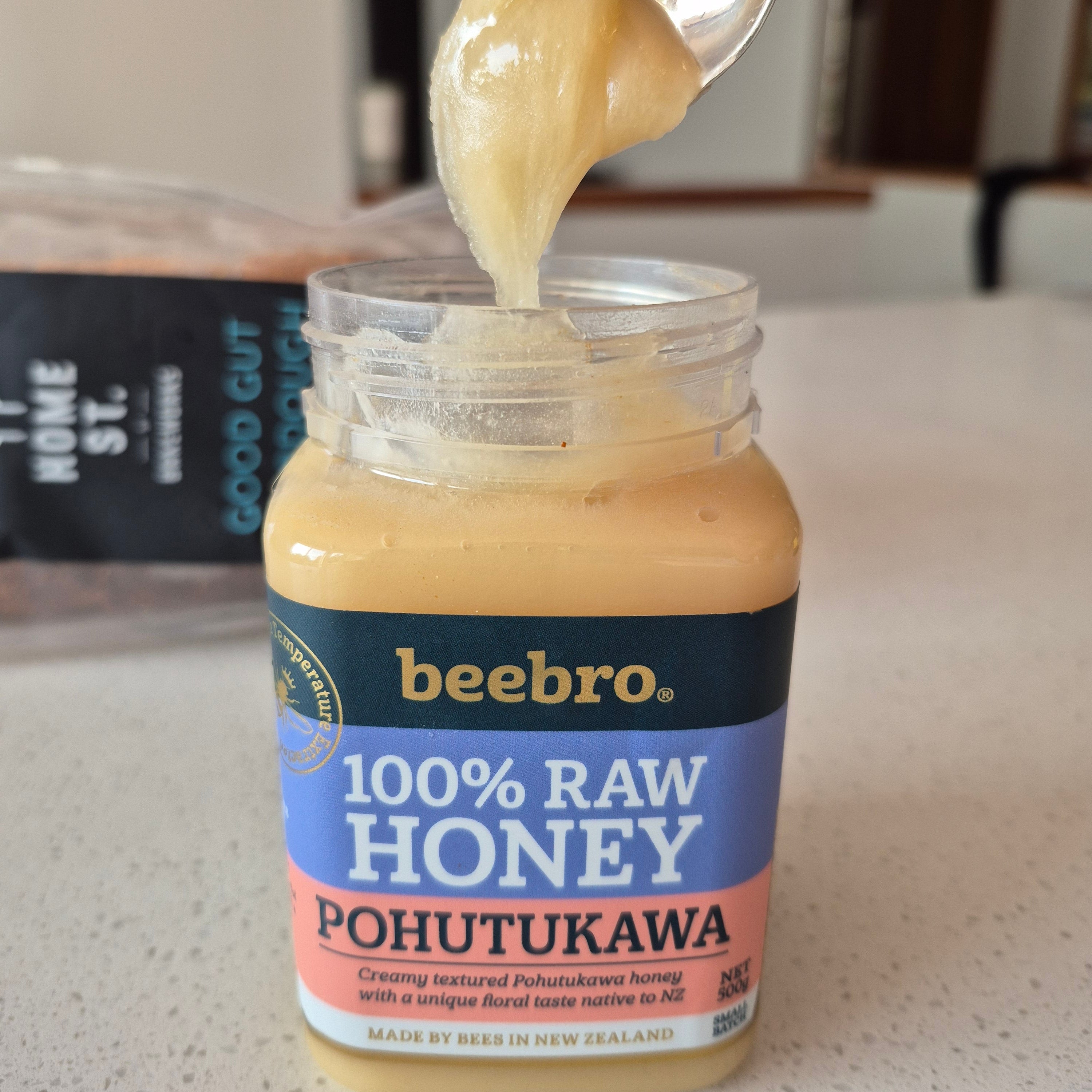 Jar of beebro honey with a spoonful of honey on a countertop